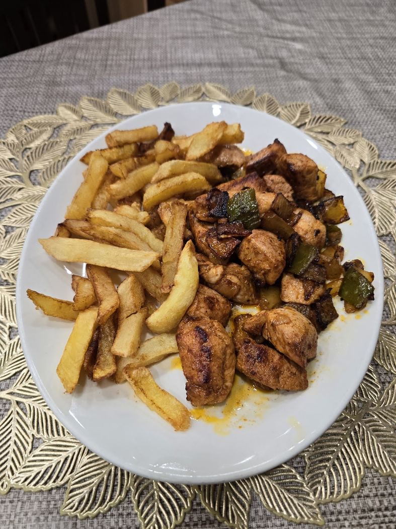Dados de pollo salteados con pimientos y patatas fritas caseras, un plato clásico del menú.